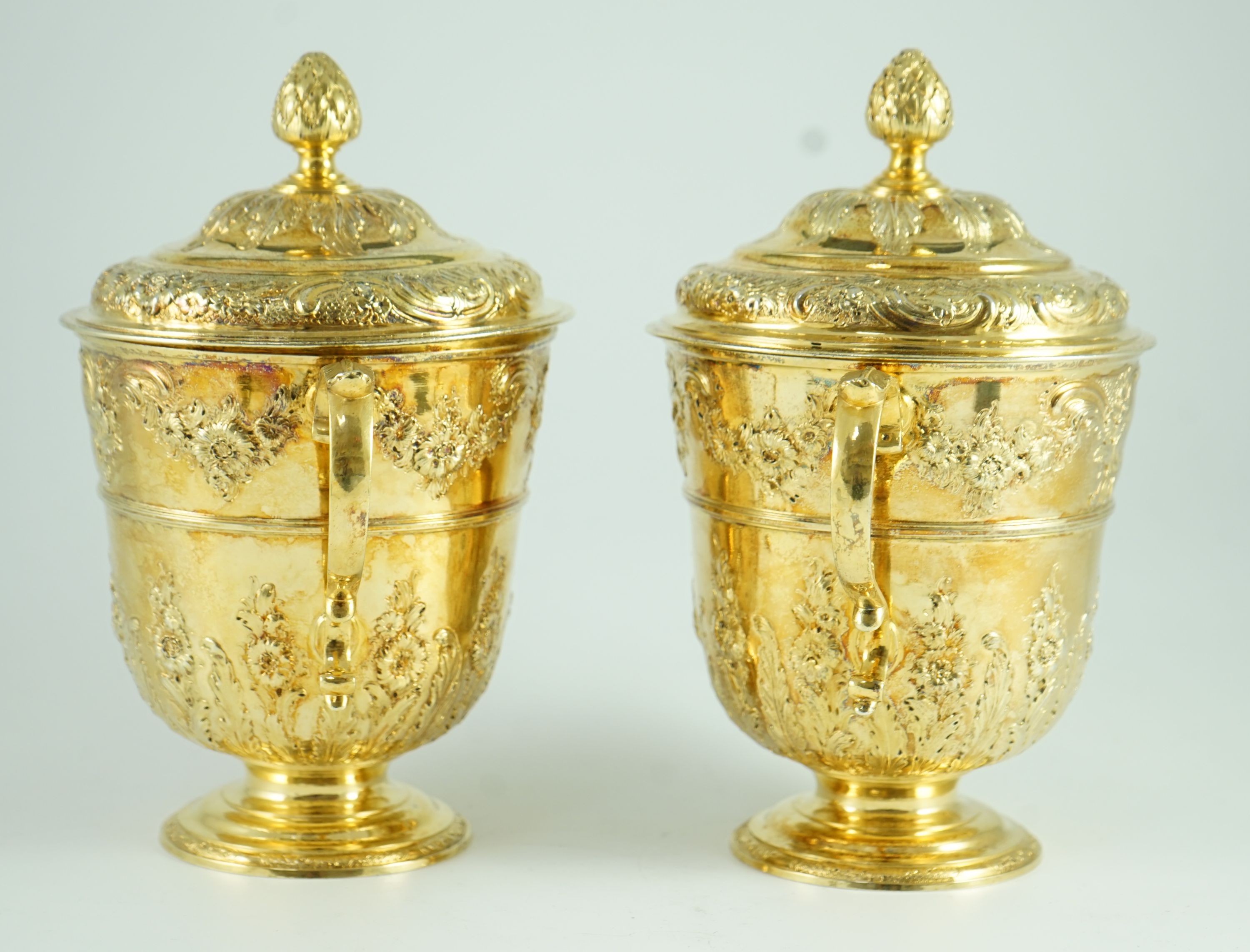 A good pair of George II embossed silver gilt two handled pedestal cups and covers, by Benjamin Gignac